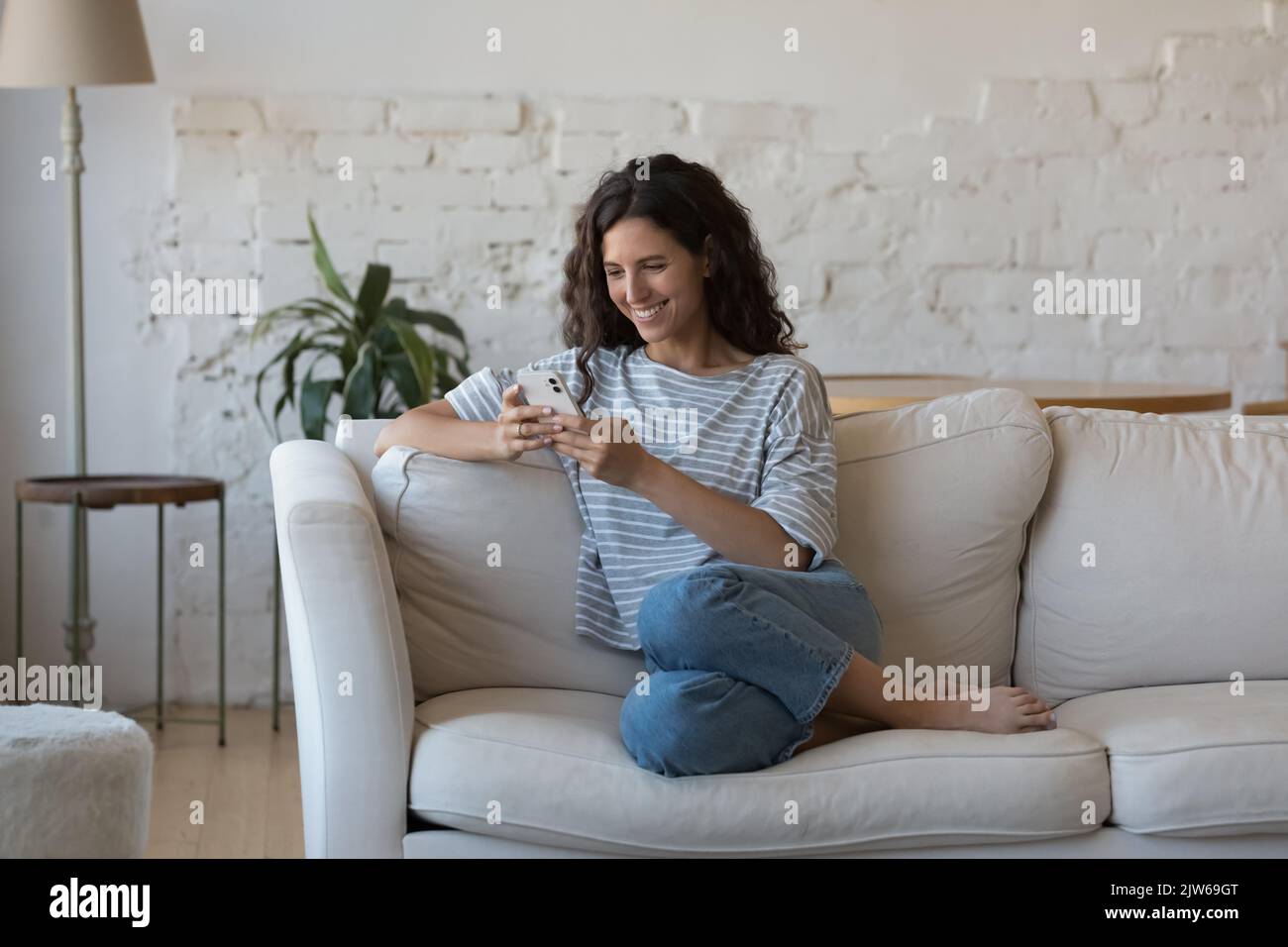 Beautiful woman sit on sofa use smartphone send messages Stock Photo
