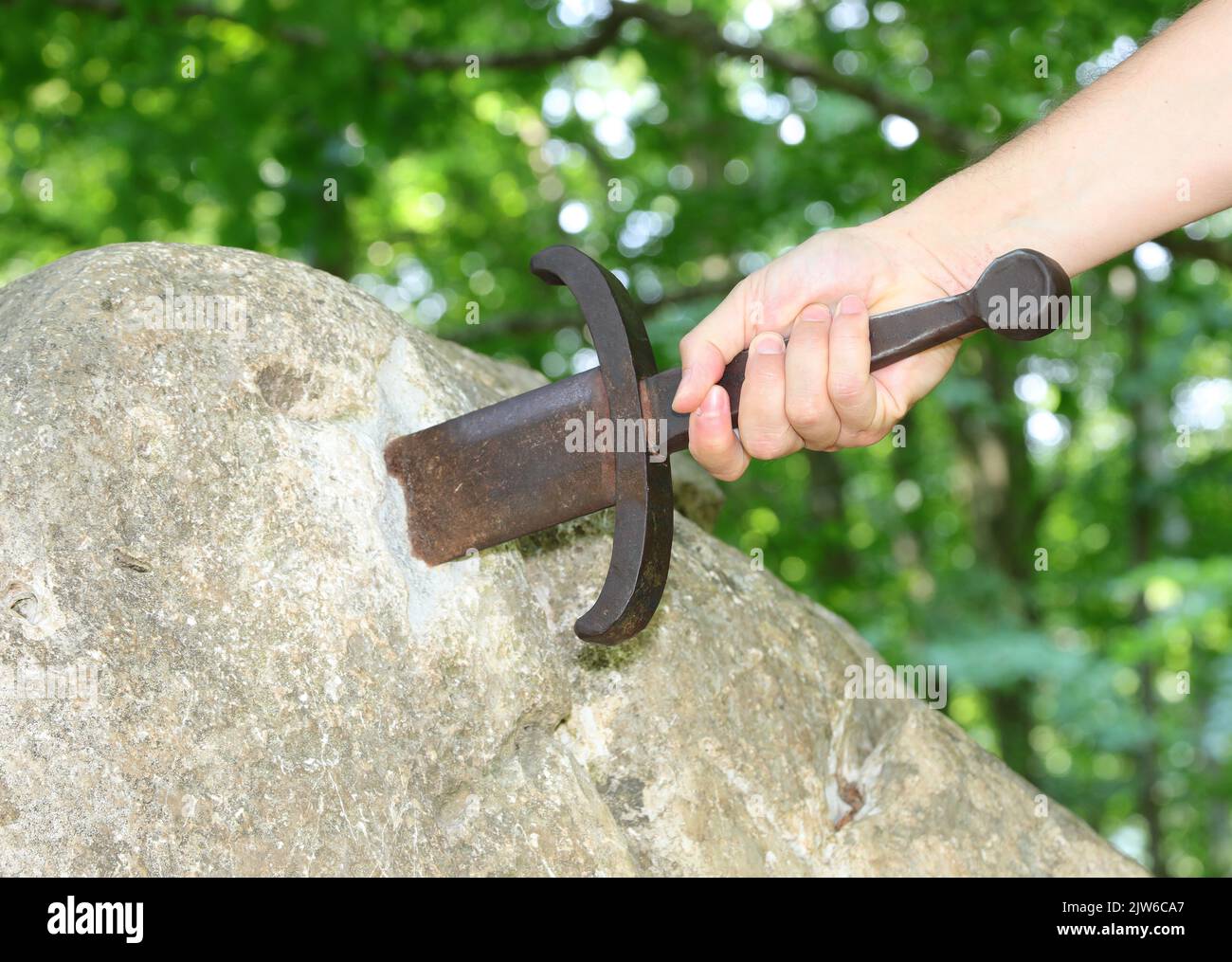 hand of the knight who tries to extract the Excalibur Sword embedded in the rock in the middle of the enchanted forest Stock Photo