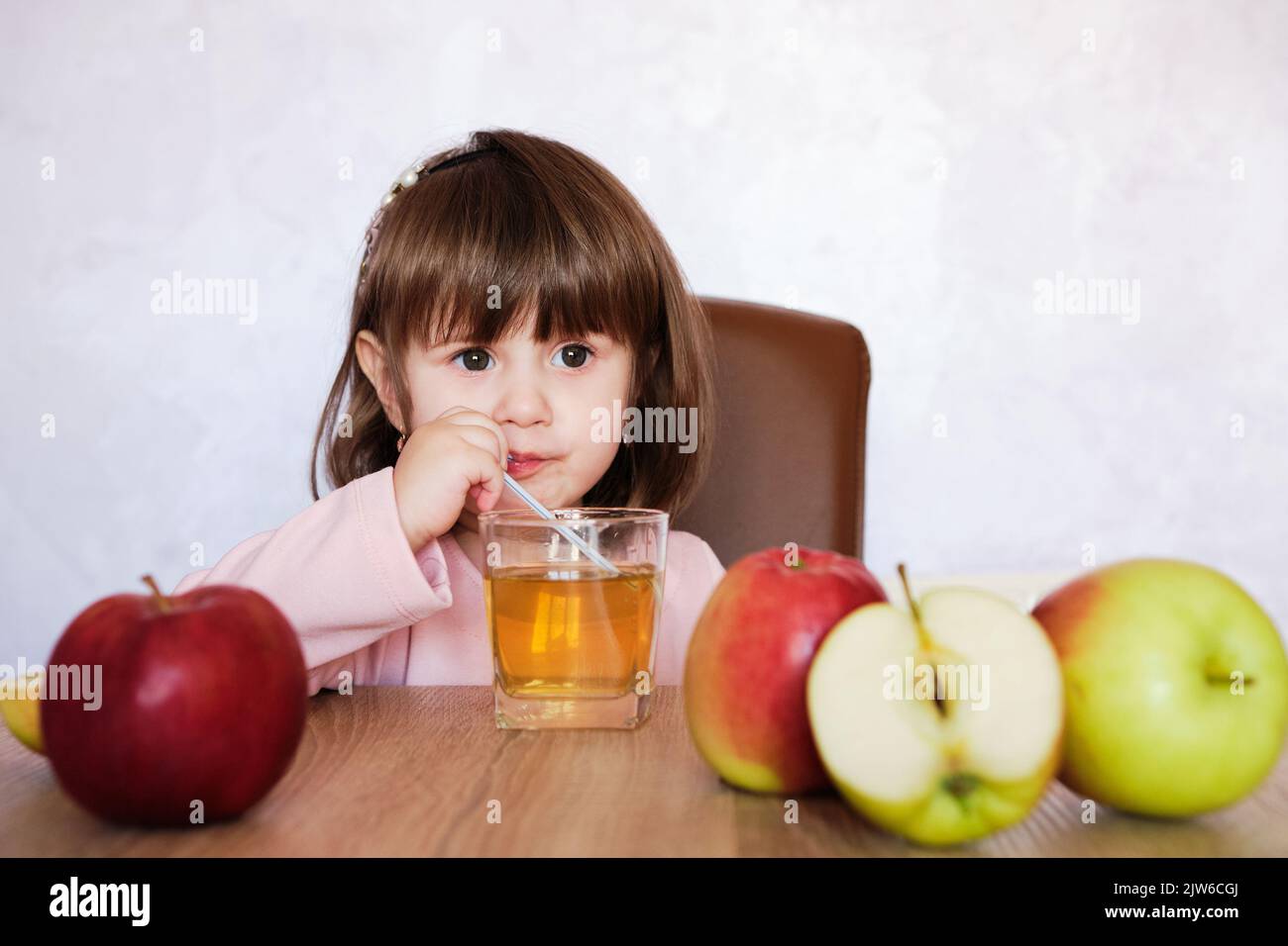 Cute little girl drinks apple juice using drinking straw. Baby girl