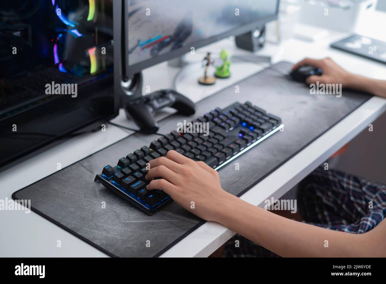 selective focus of a teenager hands playing on a gaming computer, with a black keyboard on a large gray mouse pad, addition to video games Stock Photo