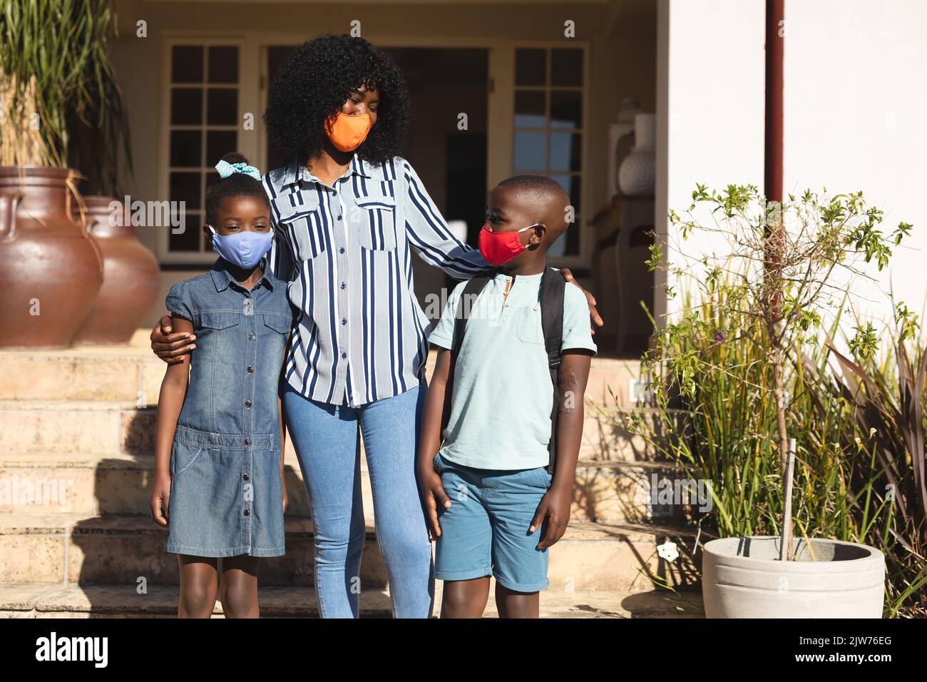 African american woman and daughter and son wearing face mask standing outdoors on a bright sunny da Stock Photo