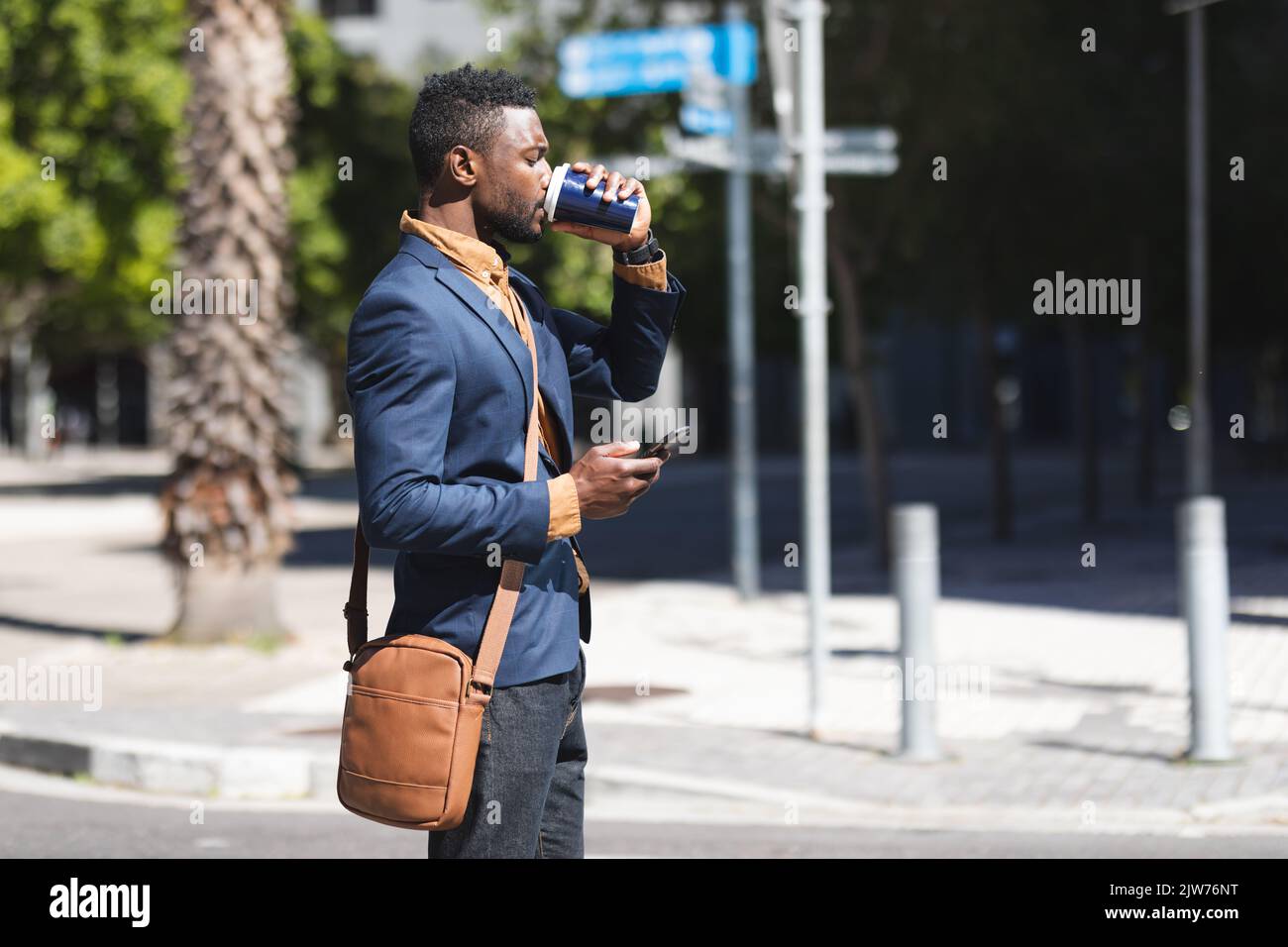 African american man standing using smartphone and drinking coffee Stock Photo