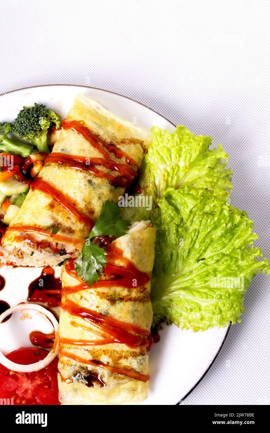 Delicious fried rice wrapped in omelet egg with sauce, ketchup, and lettuce Stock Photo