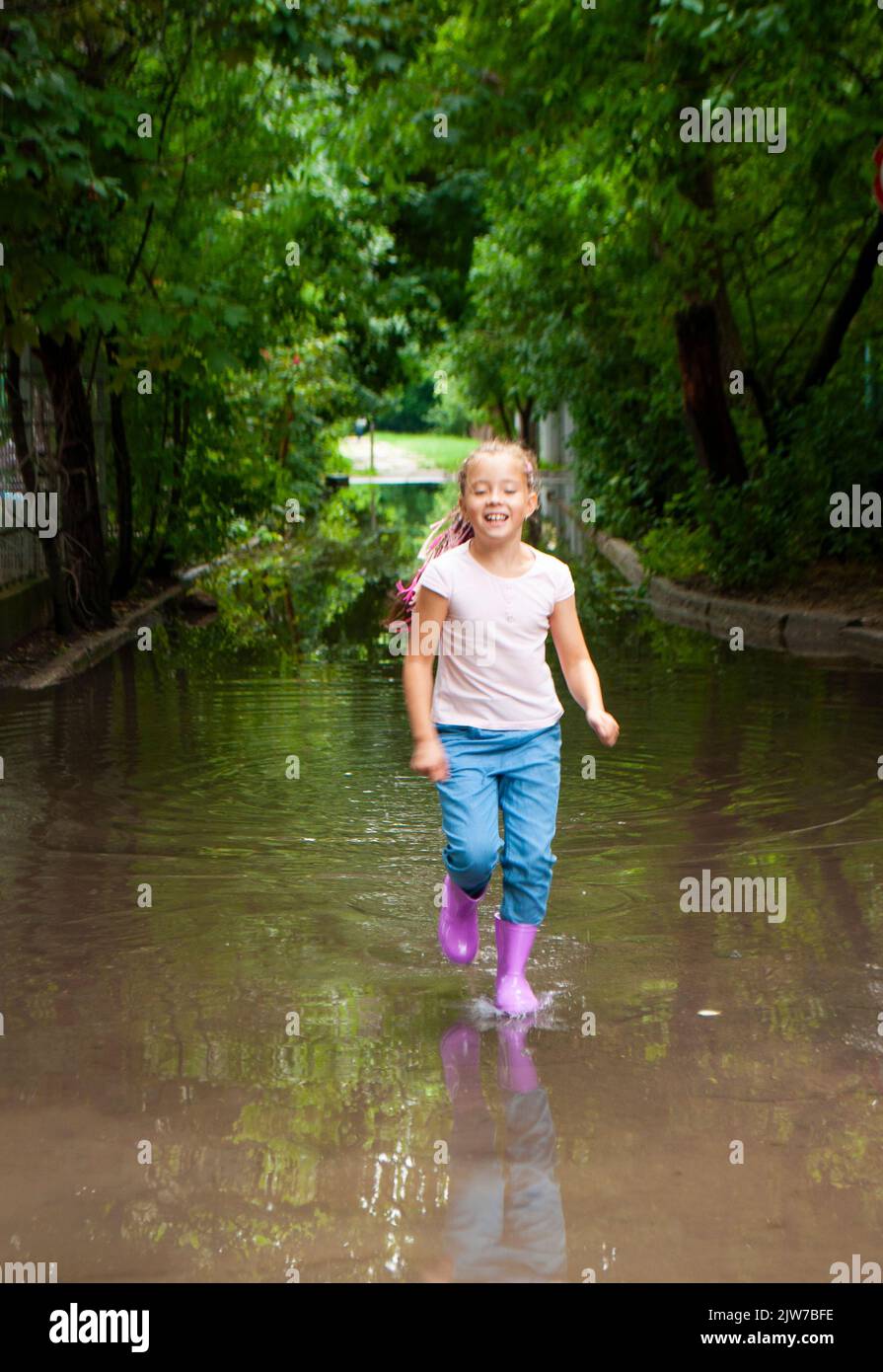 A happy braided girl in rubber boots is jumping in muddy puddles Stock ...