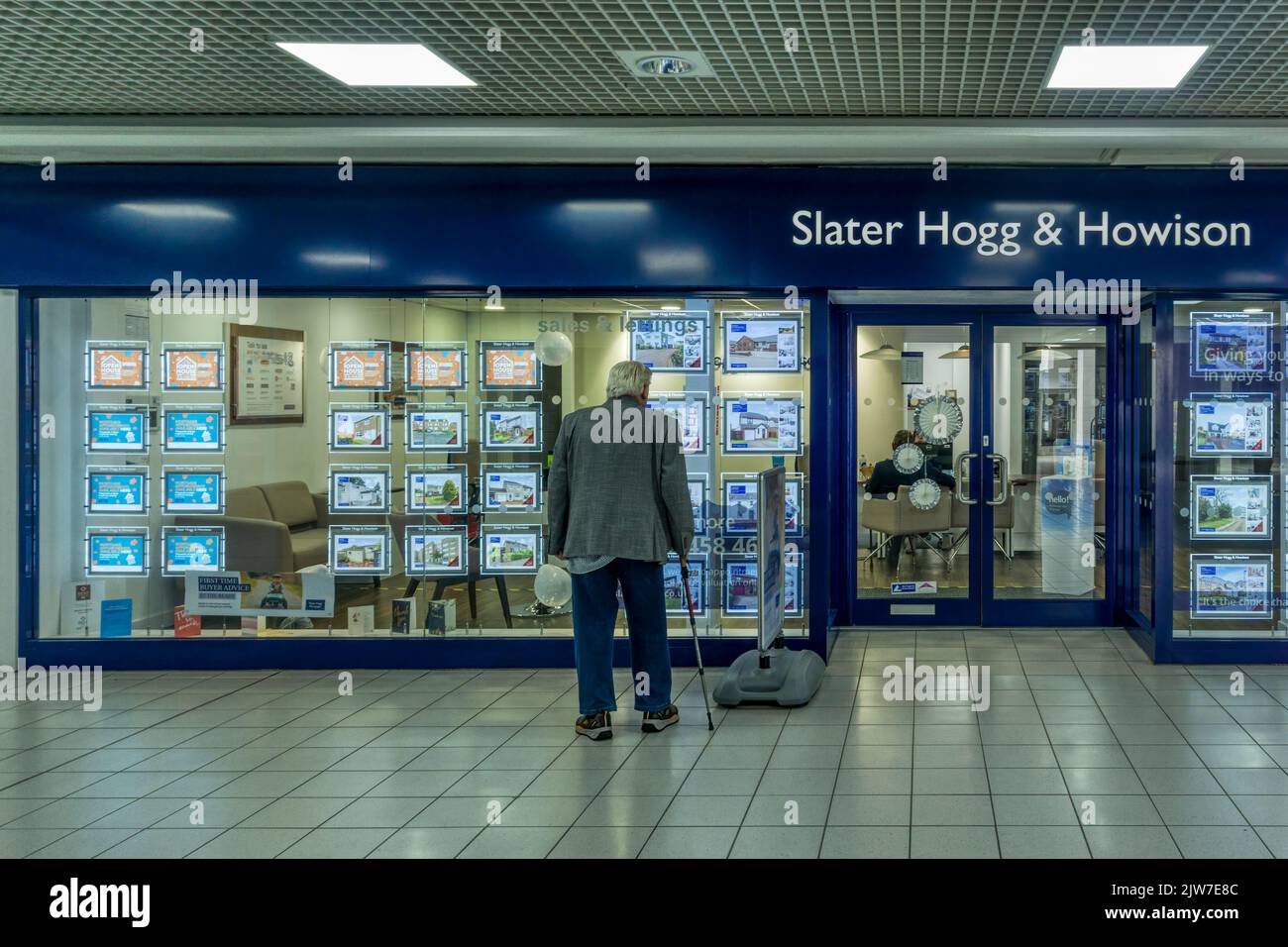 Single senior man looking at properties in the window of an estate agents in The Centre shopping mall in Cumbernauld New Town. Stock Photo