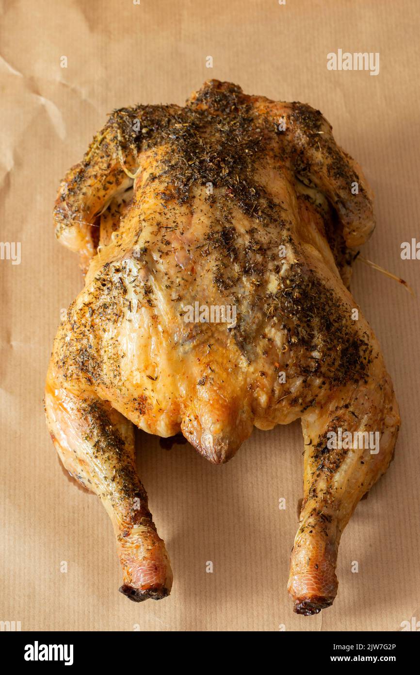 Whole chicken coated in mixed herbs roasted in an oven. On a brown