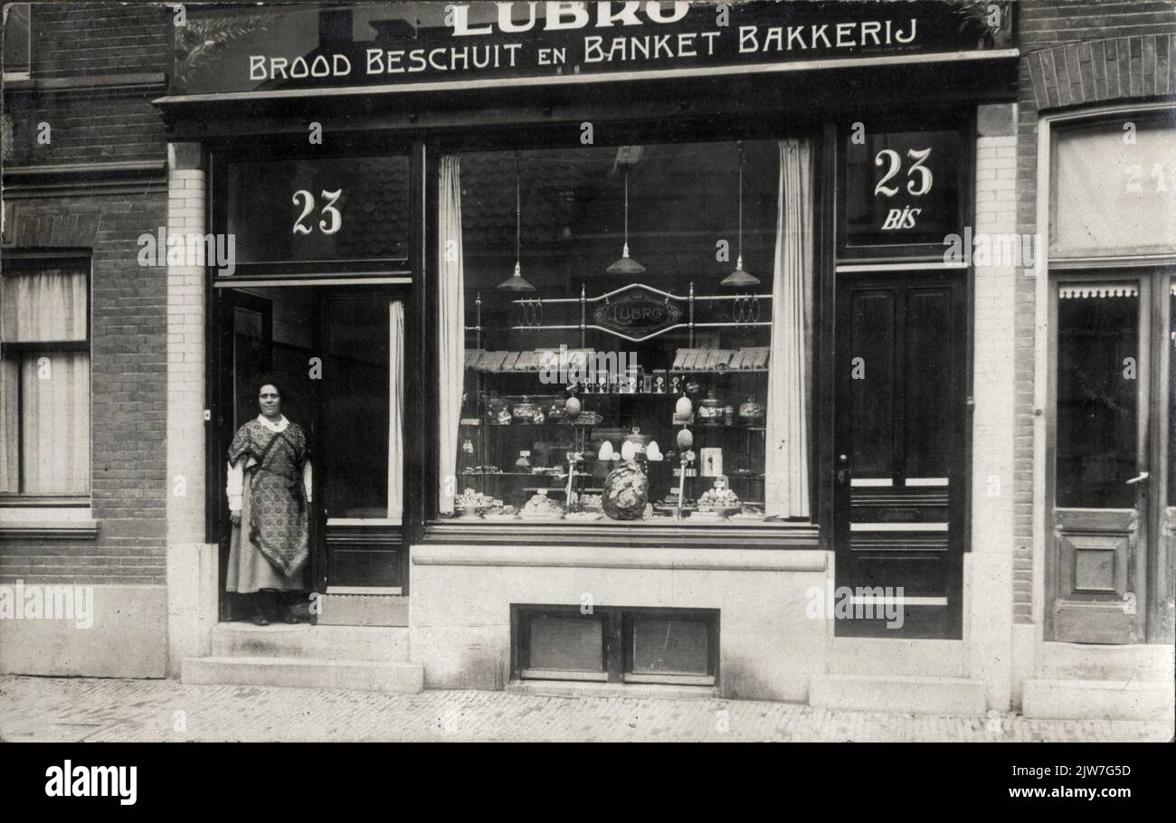 View of the shop door of Winkel no. 8 of the "Lubro Brood- en Banketbakkerijen" (Mgr. Van De Weteringstraat 23 - 23bis) in Utrecht; The unknown store keeper is in the doorway. Stock Photo