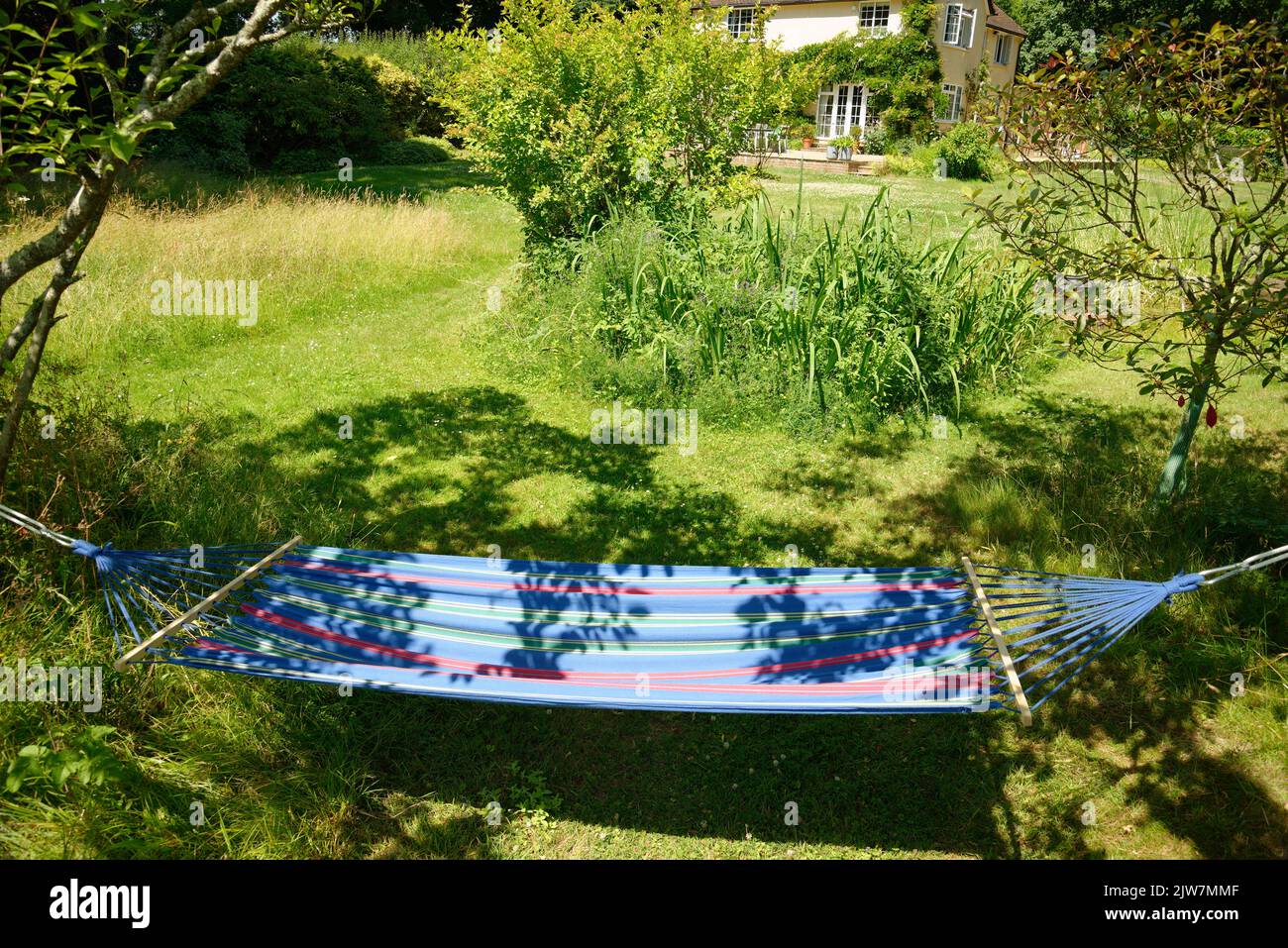 A garden hammock in summer. Relax in suspended comfort in a soft fabric hammock in dappled sunlight. Stock Photo