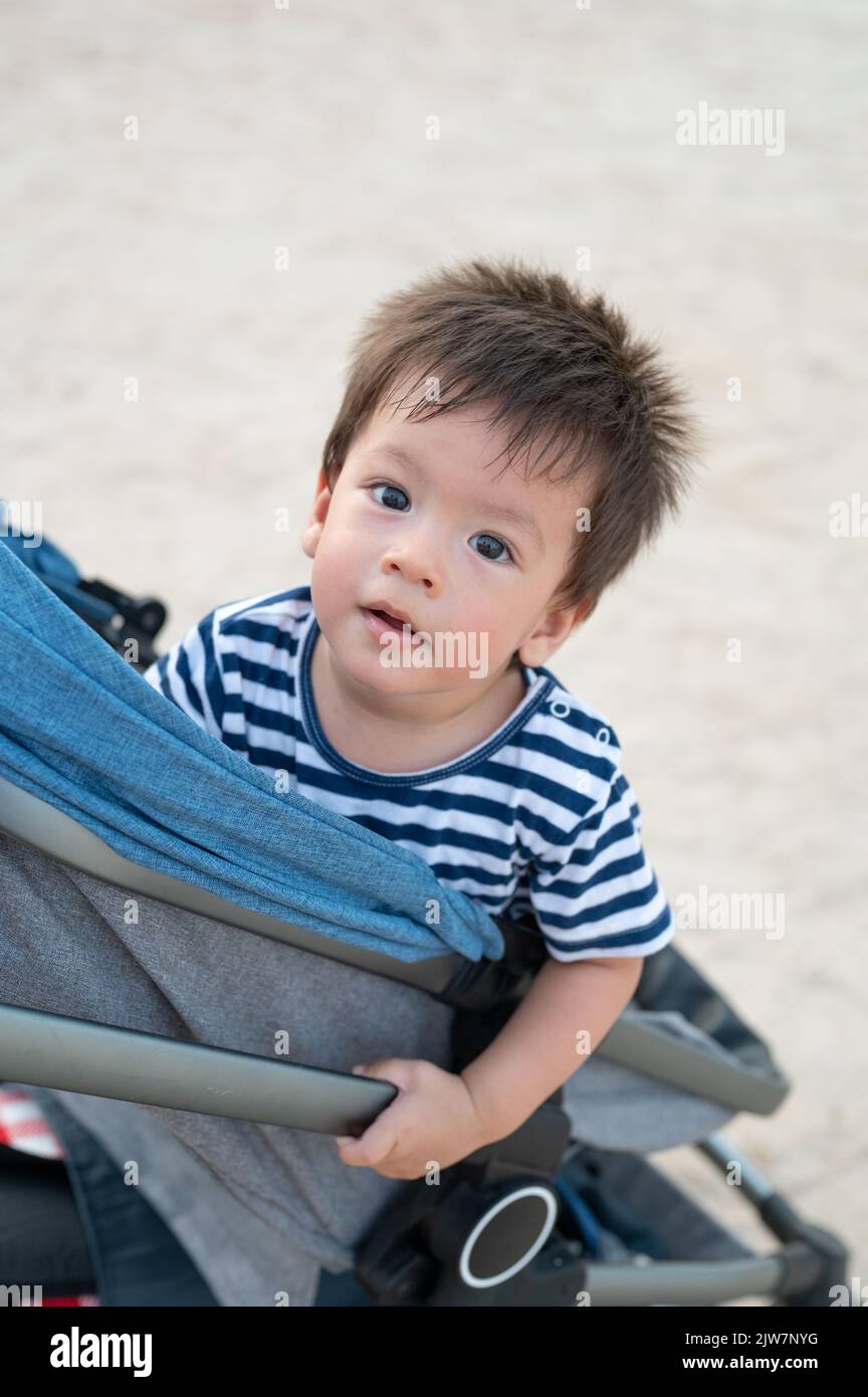 Baby boy sitting in the stroller on the beach by the seaside on the