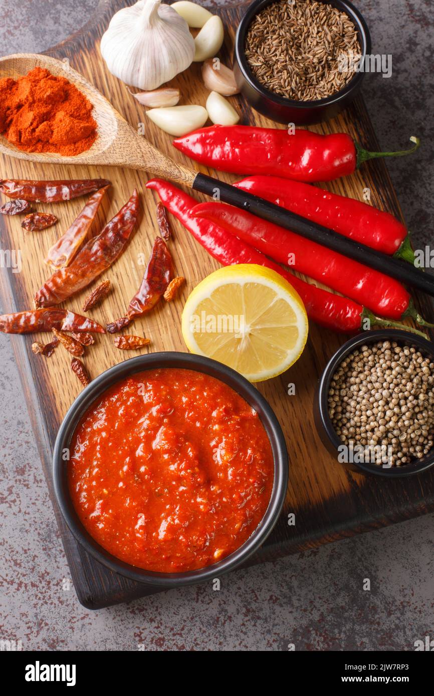 Harissa Paste North African spicy red sauce to add heat to dressings, sauces, soups in bowl on wooden board with ingredients closeup. Vertical top vie Stock Photo