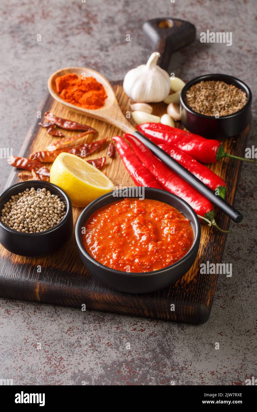 Harissa Paste North African spicy red sauce to add heat to dressings, sauces, soups in bowl on wooden board with ingredients closeup. Vertical Stock Photo