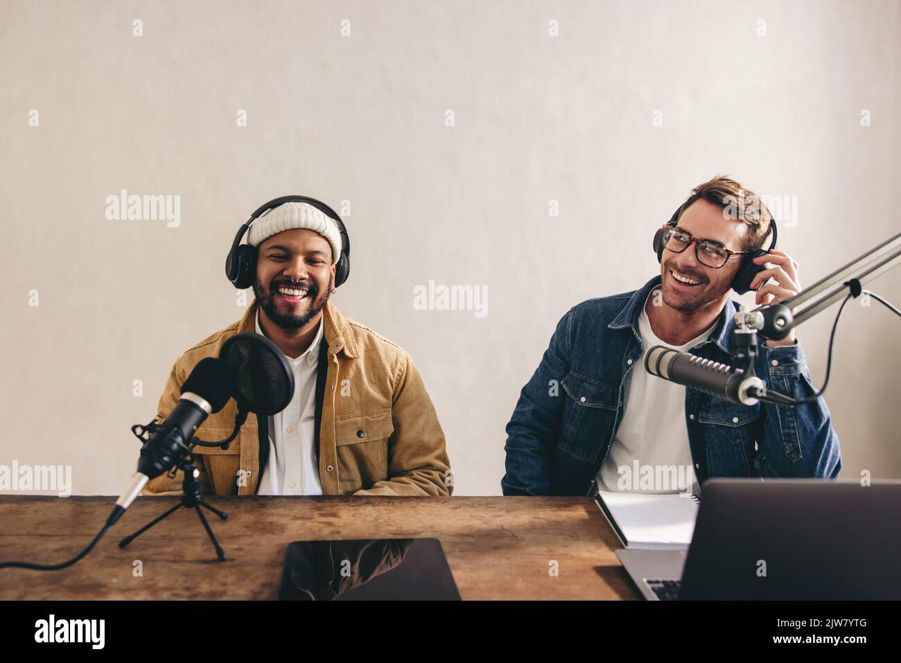Two happy radio presenters having a good time on air. Young men smiling happily while recording an audio broadcast in a studio. Cheerful content creat Stock Photo