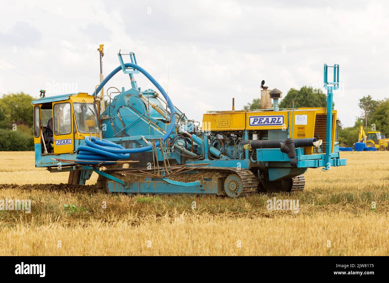 Trenching machine working in a field digging a drainage canal and laying a land drainage pipe. UK Stock Photo