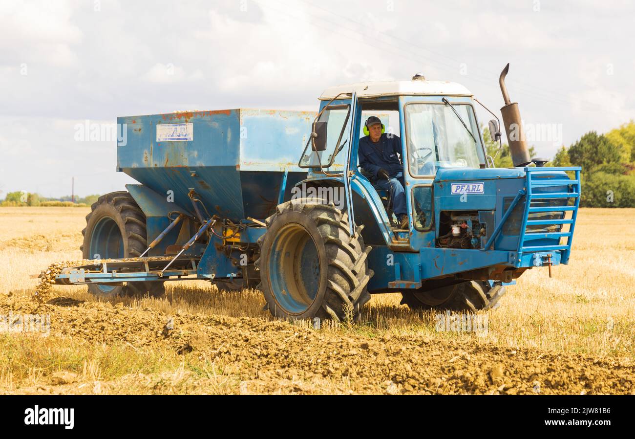 Man in a tractor depositing shingle into a newly dug drainage trench. Stock Photo