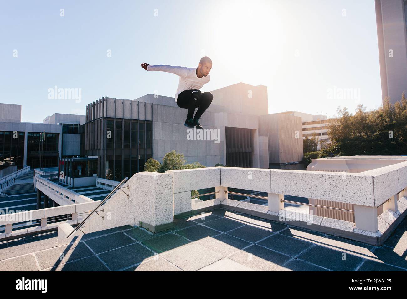 Athletic young man doing parkour tricking and freerunning over urban city background. Young sportsman practicing extreme sport activities outdoors in Stock Photo
