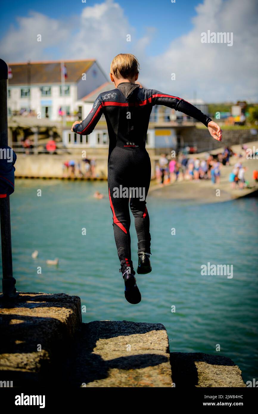 My lad taking a jump of Porthleven harbour wall into the sea. Stock Photo