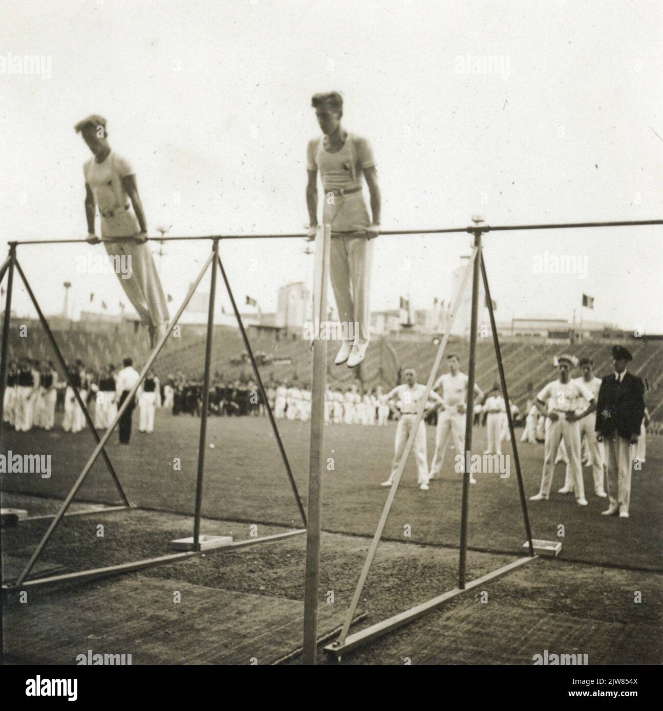 Image of an exercise on the horizontal bar with athletes of the Utrecht Gymnastics and Screen Association Bato during the gymnastics tournament in the Jubel Stadium in Brussels.n.b. The gymnastics parties were organized because of the 70-year anniversary of the Royal Belgian Turnbond and took place from 19 to 23 July in the Jubel Stadium (later Heysel Stadium and then King Baudouin Stadium). Stock Photo