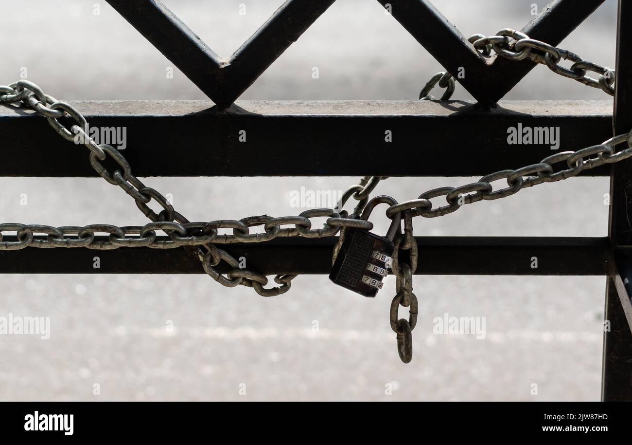 Metal lock with manual code close-up tied with chain to metal fence on light blurred background Stock Photo