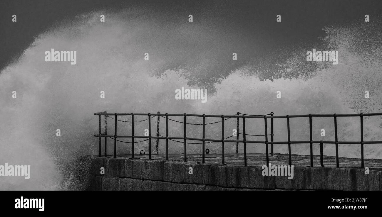 As a storm hits the coast of Cornwall, the pier at Porthleven harbour takes the force of the waves as they hit hard. Stock Photo