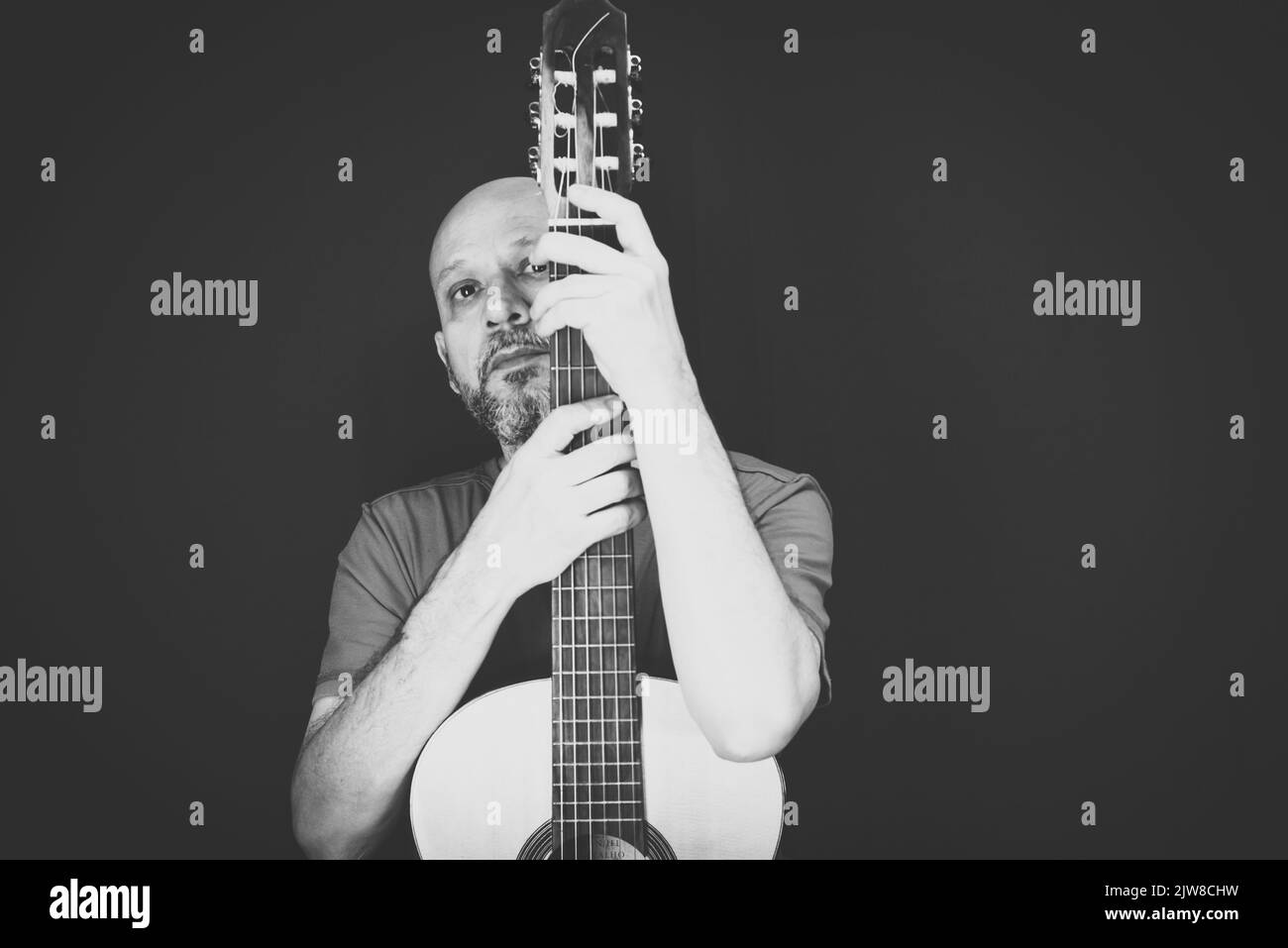 Black and white portrait. String musical instrument. Mature charismatic male guitarist. guy with beard holds guitar. bearded man in a red shirt. Music Stock Photo