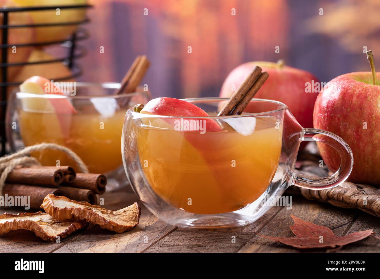 Cup of apple cider with apple slice and cinnamon stick on rustic wooden table with autumn background Stock Photo