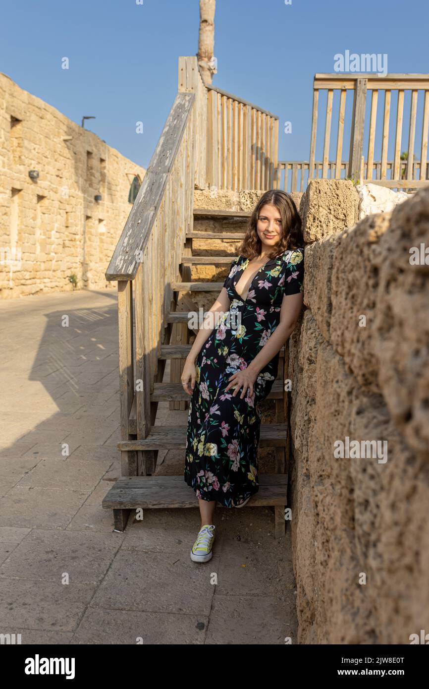 A smiling girl in a black long dress with flowers stands near the observation deck and steps against the sky Stock Photo