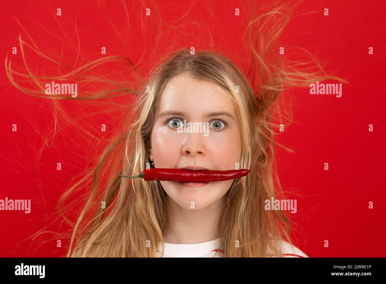 Shocked, expressed, surprised blonde woman with chili pepper in mouth and flying electrified hair locks. Copy space Stock Photo