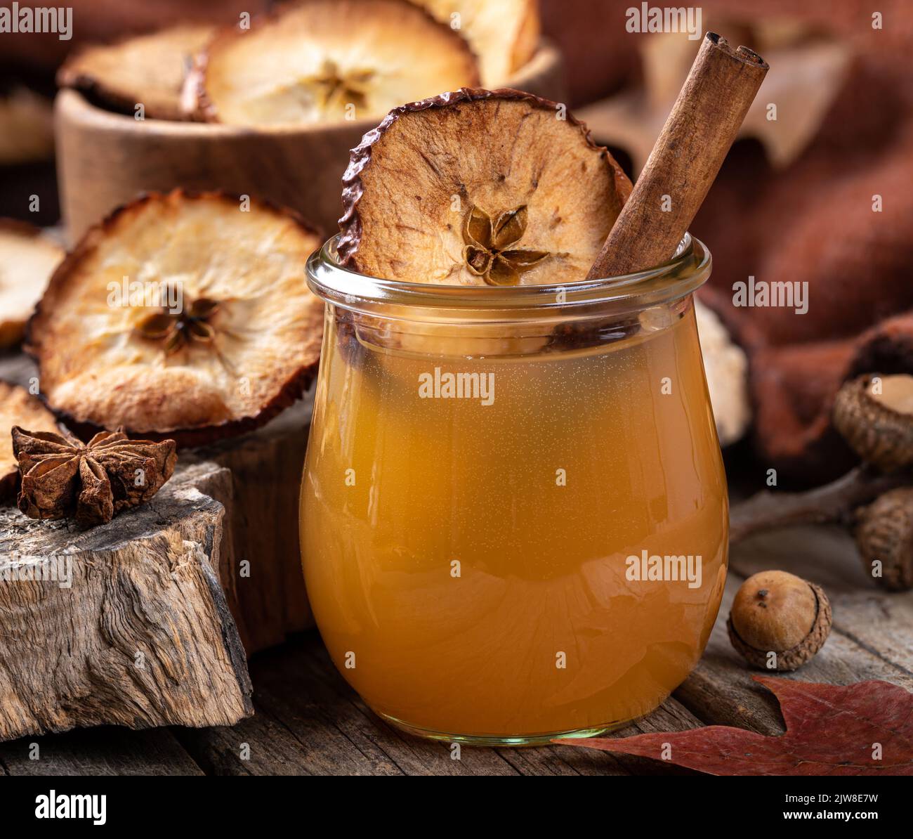 Closeup of glass of apple cider with cinnamon stick and dried apple chip on a rustic wooden table Stock Photo