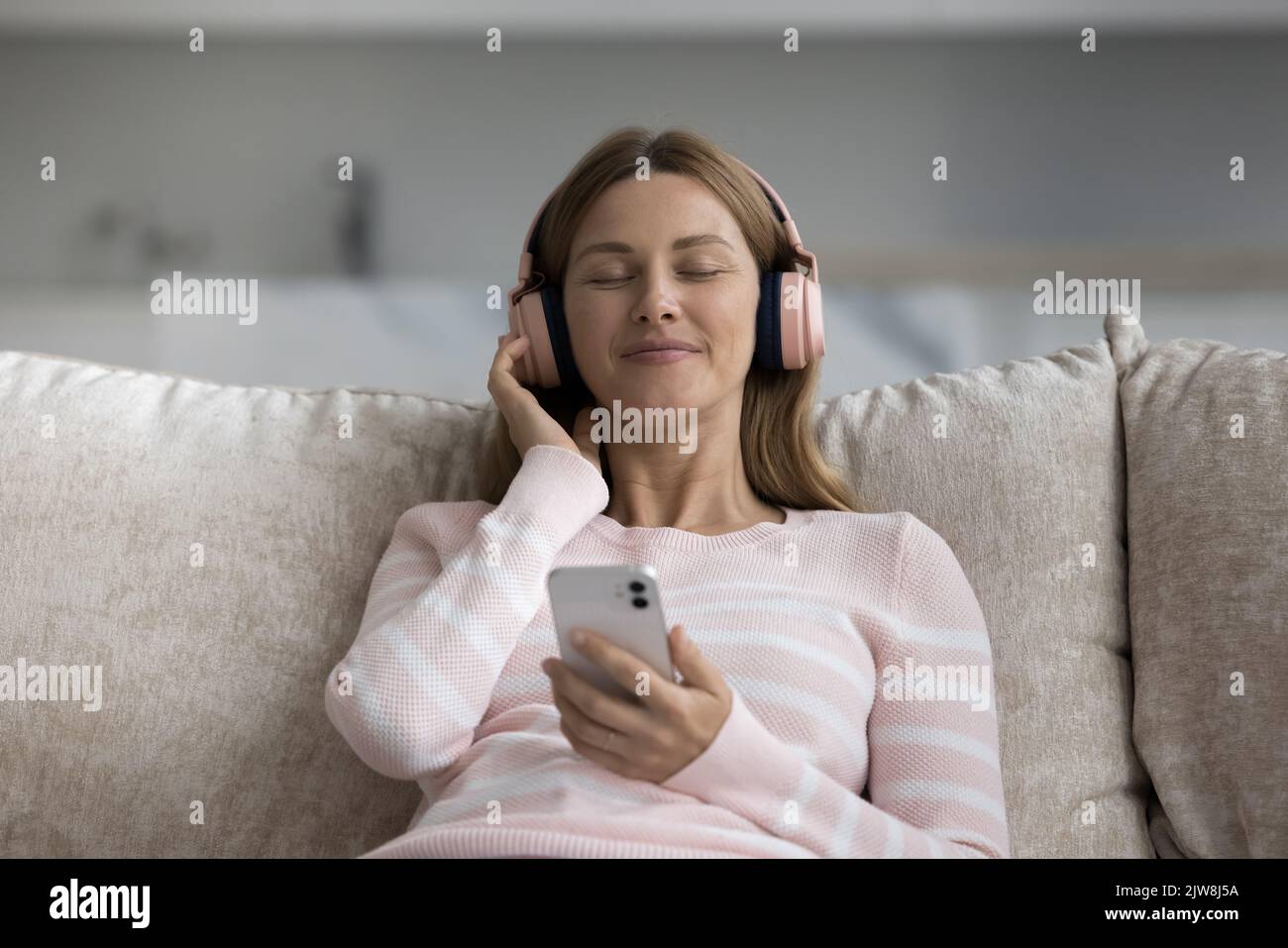 Cheerful woman in big wireless pink headphones holding smartphone Stock Photo