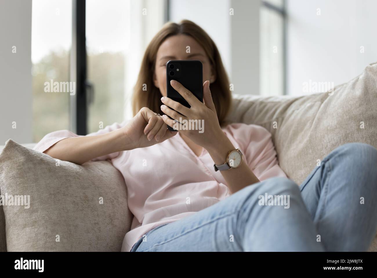 Young millennial unrecognizable smartphone user woman resting on home sofa Stock Photo