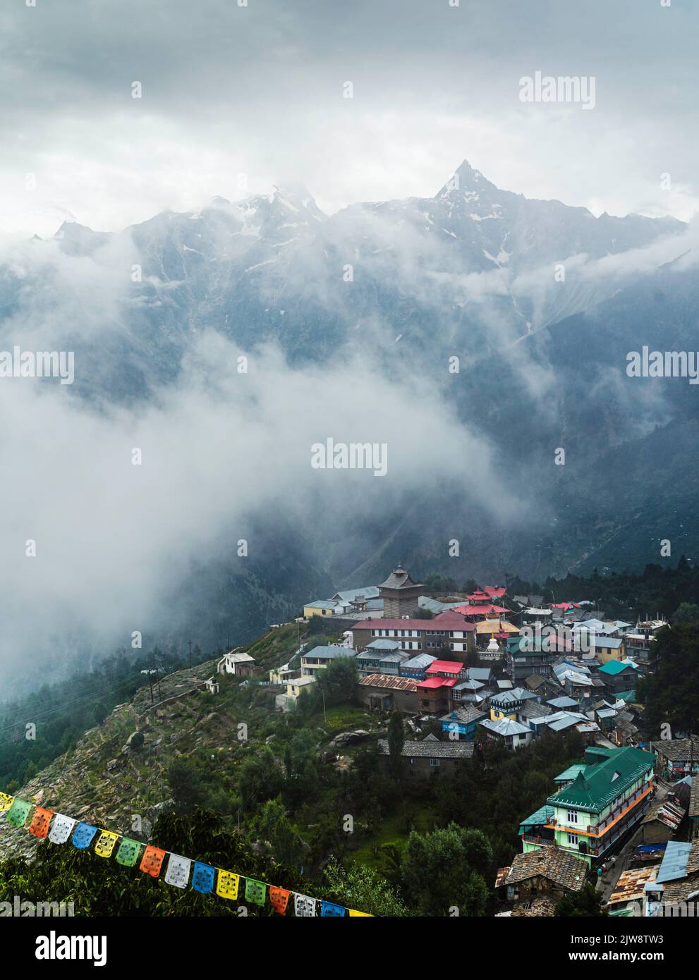 Elevated view of Kalpa village and Himalayas with sharp ridges as backdrop on a misty morning in summer in Kalpa, Himachal Pradesh, India. Stock Photo
