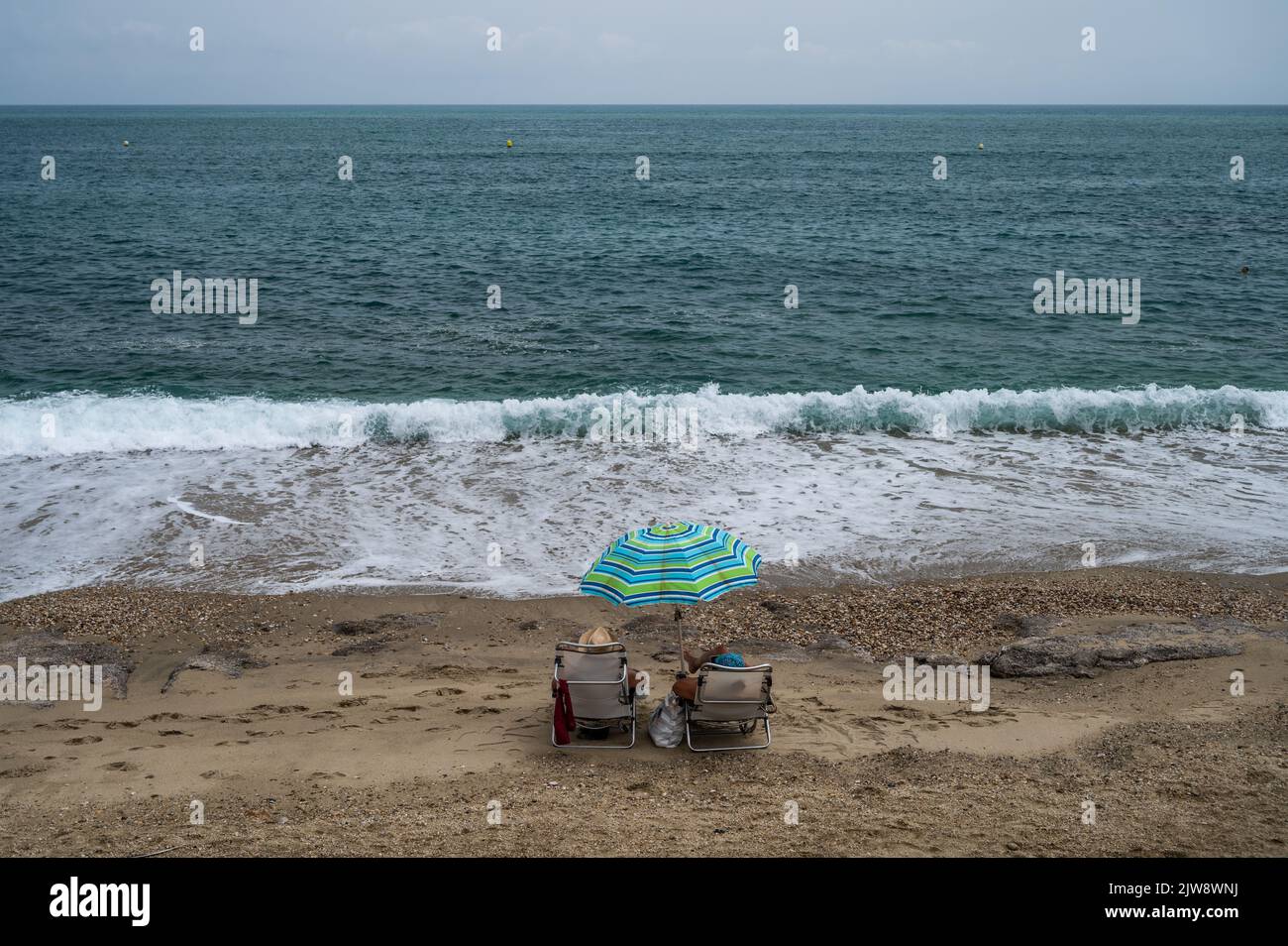 A couple of tourists sitting at the shore in Garrucha Beach, in the province of Almeria, south of Spain, during a summer day. Stock Photo
