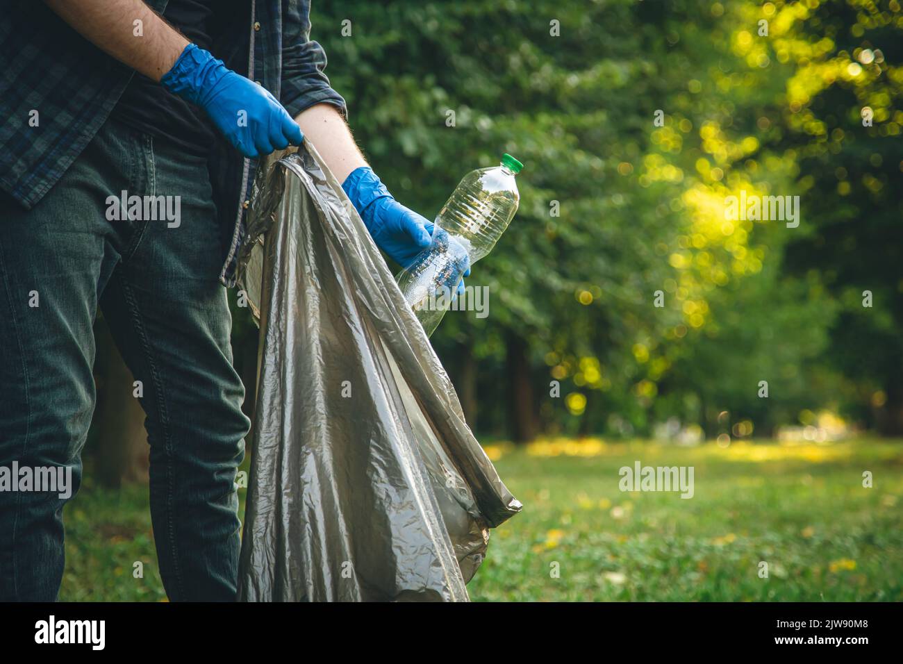 A man cleans up the forest, throws a bottle into a trash bag, closeup
