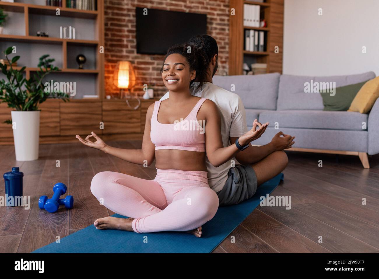 Glad calm young african american couple in sportswear with closed eyes meditation, practice yoga on mat Stock Photo