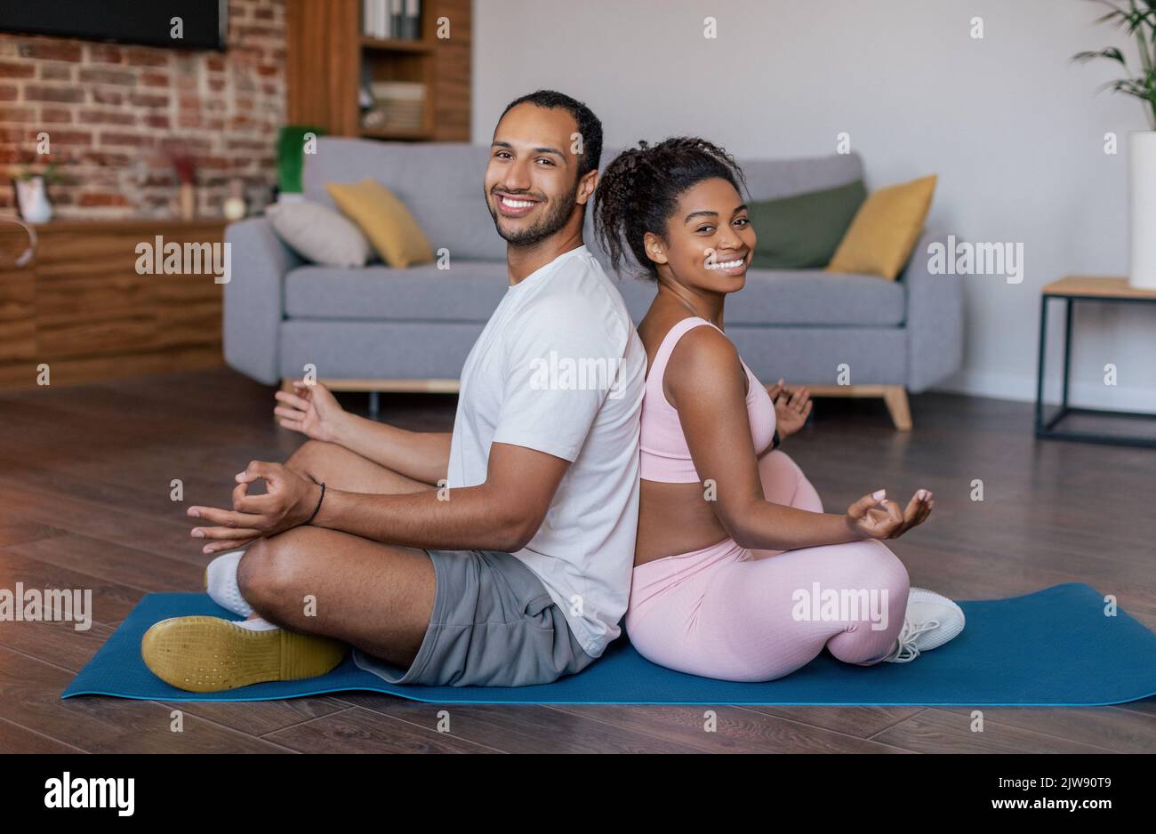 Happy young african american guy and lady in sportswear practice yoga, meditation, back to back Stock Photo