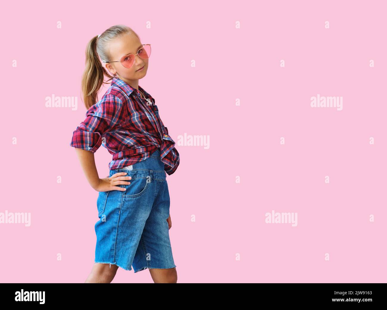 cool kid girl in pink sunglasses posing against pink background Stock