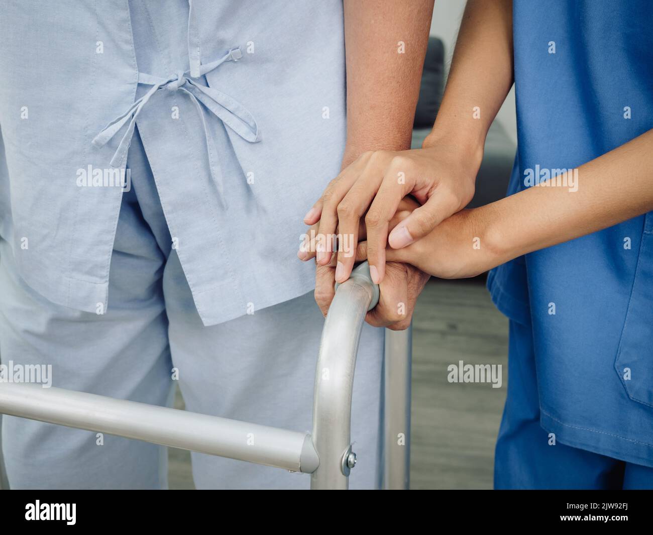 Close-up of nurse's hands, assistant in blue suit holding elderly or older woman's hands for support and care while the older patient tries to walk wi Stock Photo