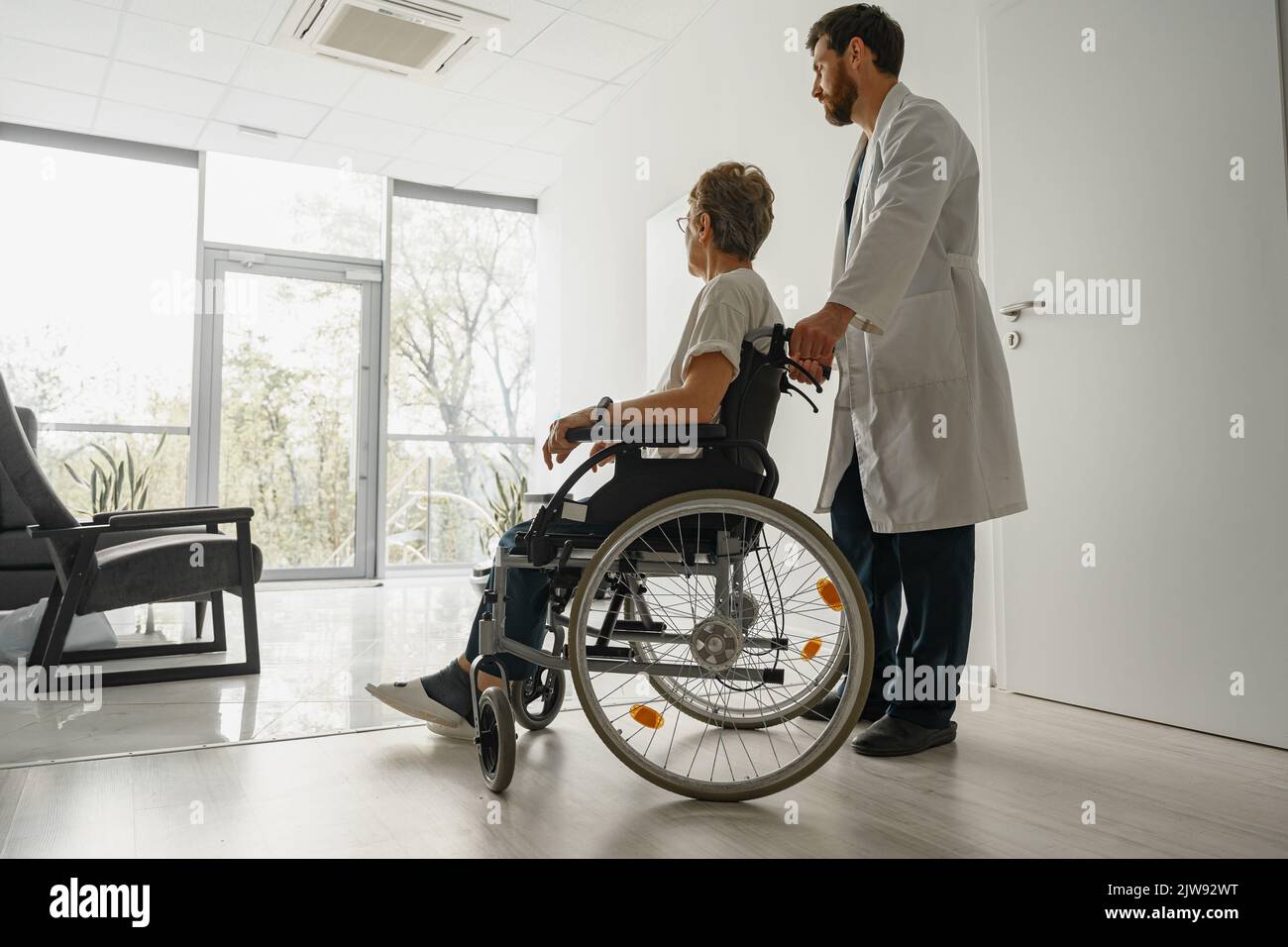 Professional male doctor carrying female patient on wheelchair in