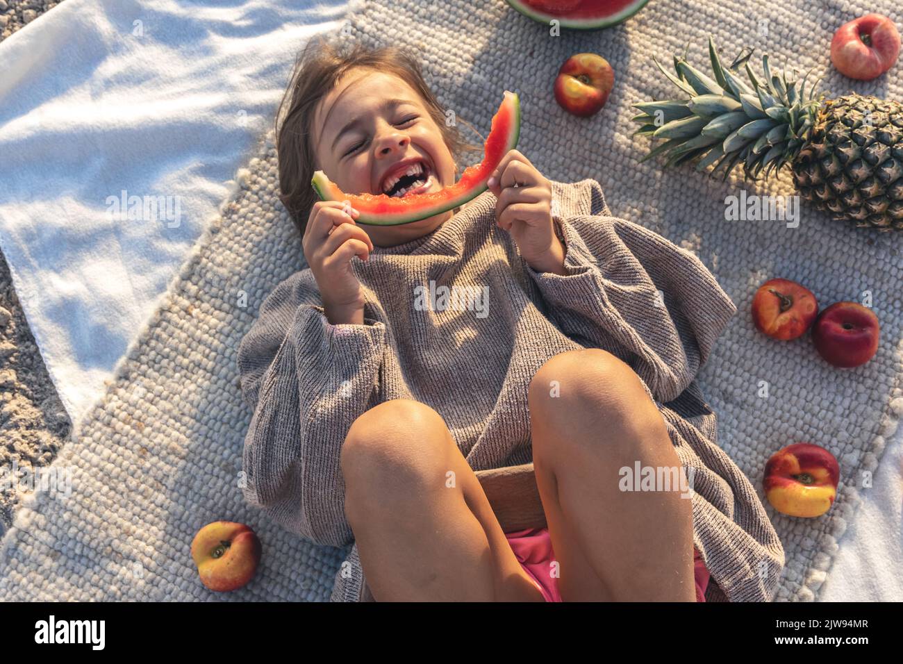 Little girl eats fruit lying on a blanket on the beach Stock Photo Alamy