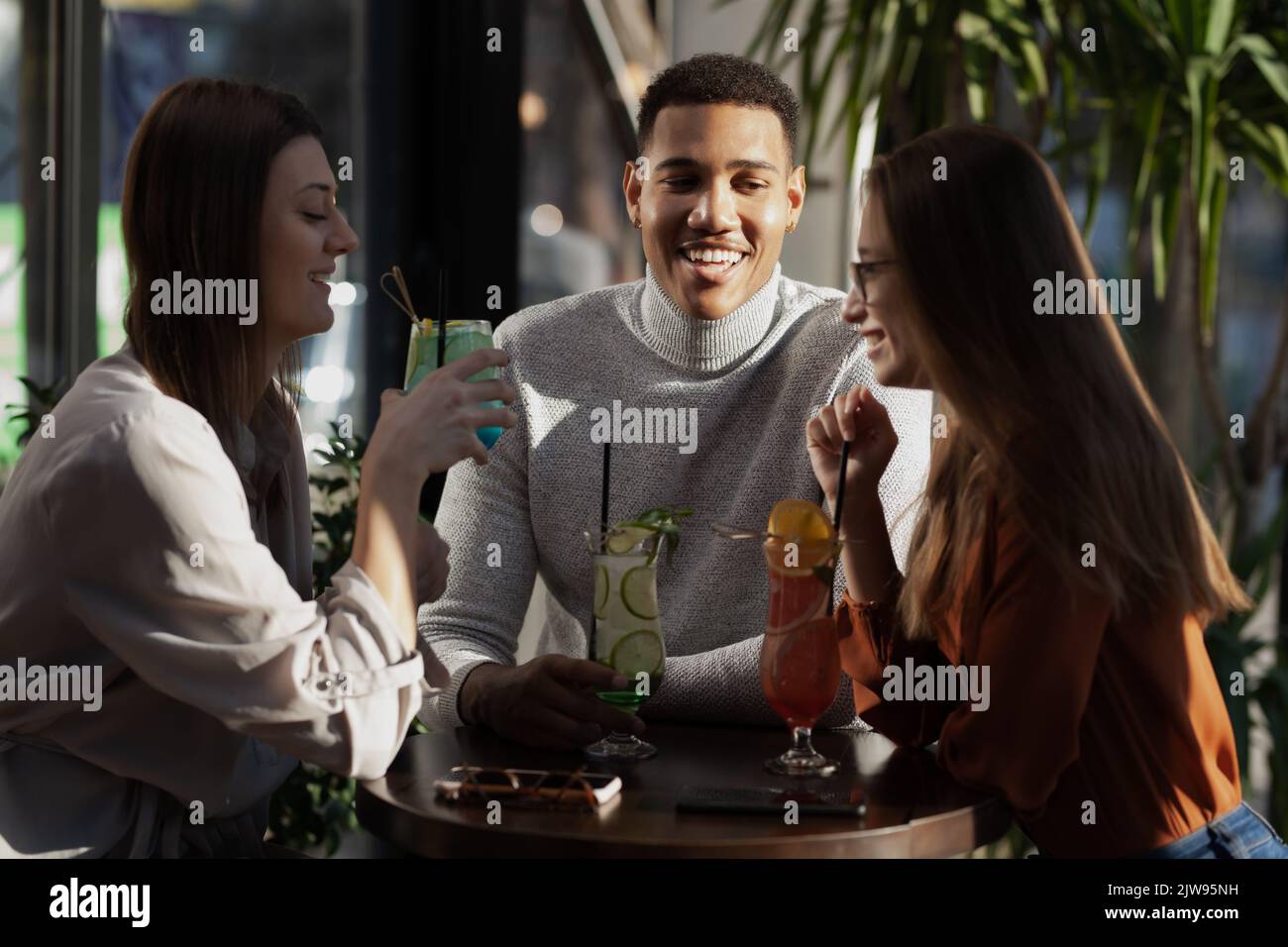Three multiracial friends in a bar cheering. After work party with cocktails after successful work day. Stock Photo