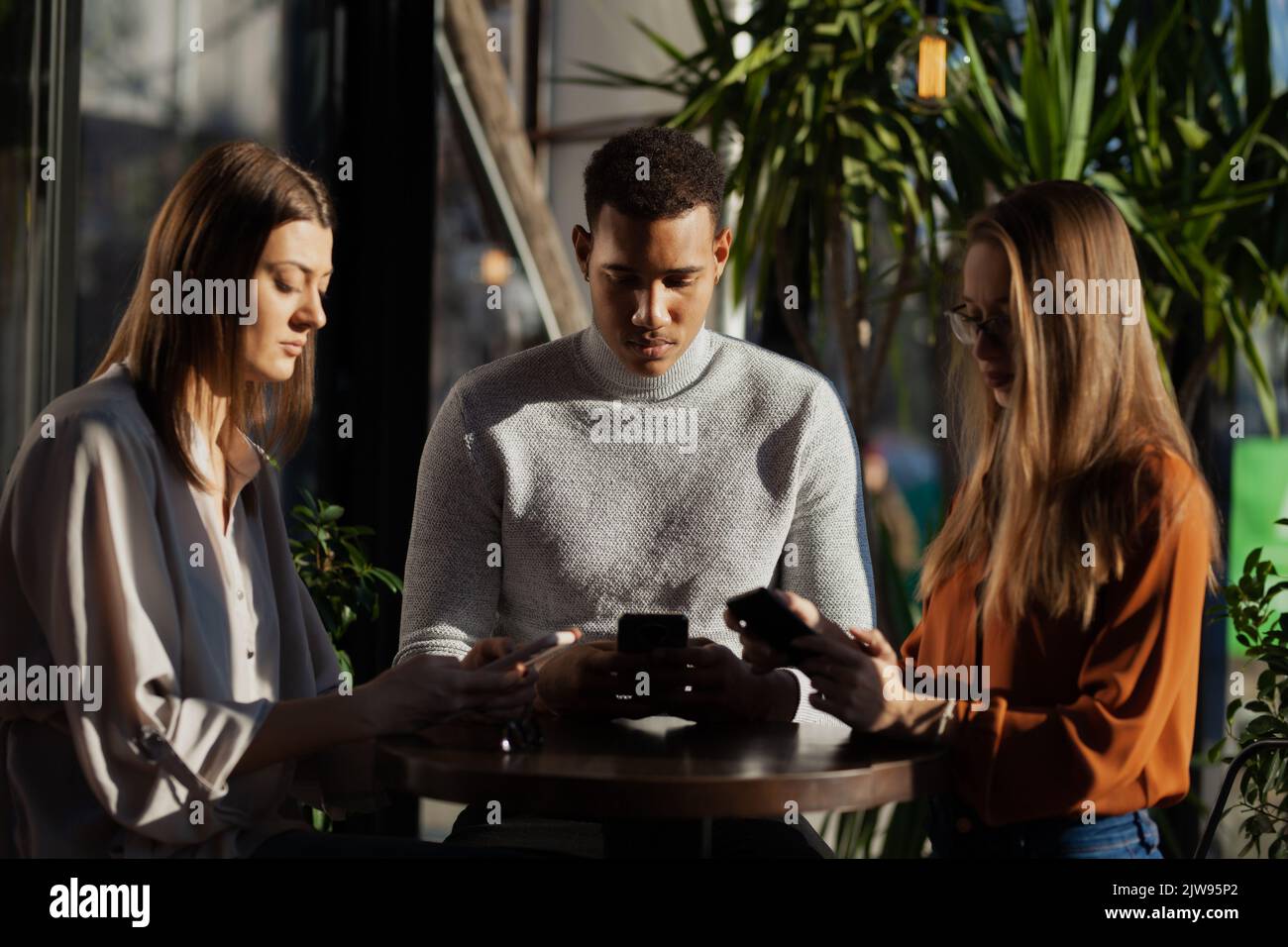Three friends in a cafe bar using phone. Looking at smartphones unconscious about the surroundings. Stock Photo