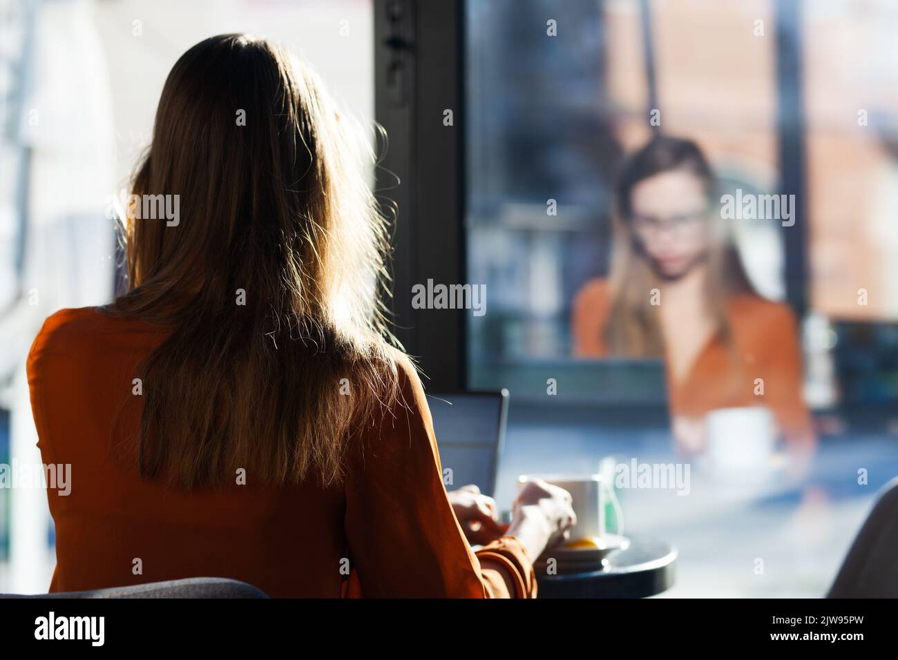 Young businesswoman in a cafe bar or restaurant. Freelancer girl working on laptop and having tea sitting at a window table. Stock Photo