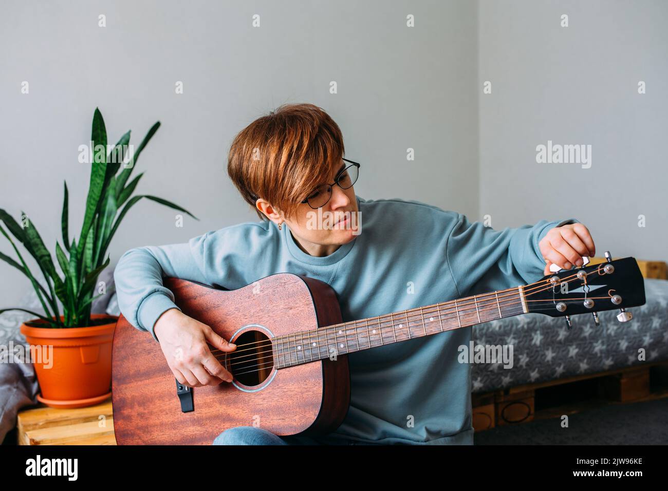 Woman with short hair enjoys playing guitar at home. Music lessons for