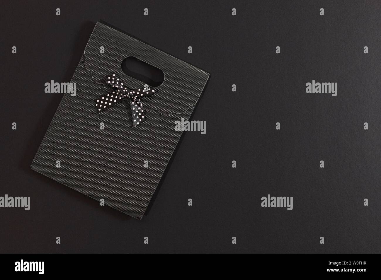 Black gift envelope with polka dot bow isolated on dark background. On one side there is empty space. Stock Photo
