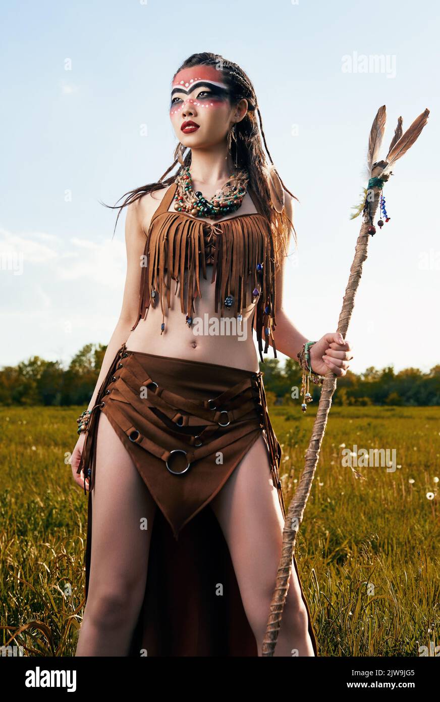 Outdoor portrait of the pretty young shamaness (witch doctor) with stick. Beautiful shaman (enchantress) in the meadow Stock Photo