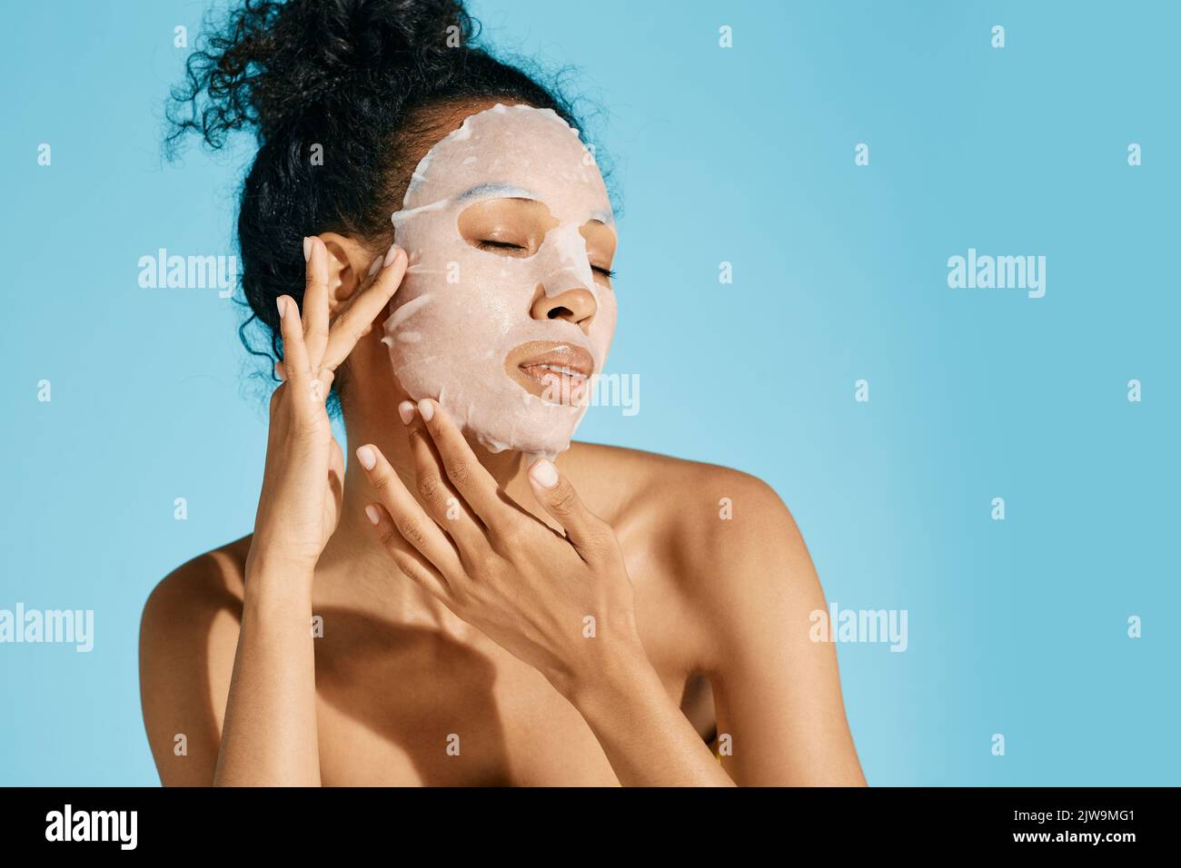 African woman portrait with moisturizing skincare mask on blue background, high quality. facial hydrating and rejuvenation procedure Stock Photo