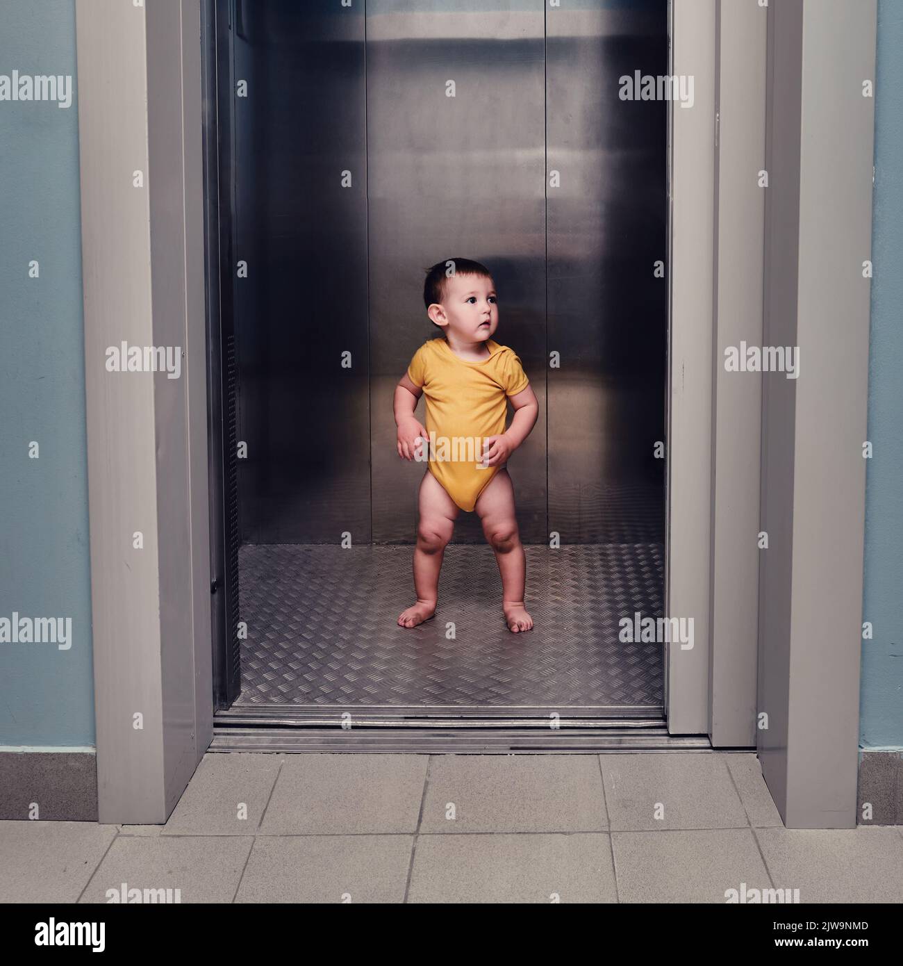 Toddler baby boy stands alone in the elevator of a residential building
