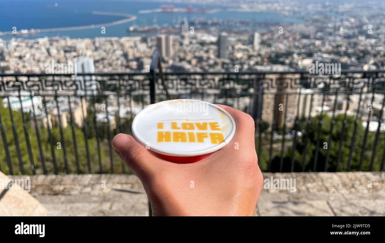 The caption I LOVE HAIFA in a cup of coffee and a view of Haifa city in the background. Stock Photo