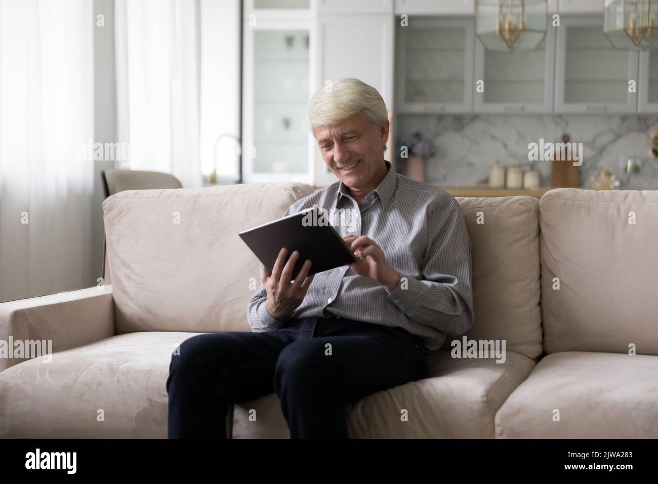 Happy senior tablet user using digital device on home couch Stock Photo