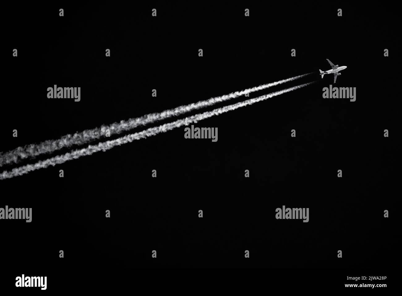 Twin-engined jetliner with contrails flying in black sky Stock Photo